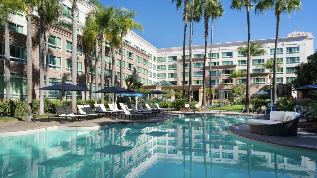 a resort pool with chairs and palm trees and a building at DoubleTree by Hilton San Diego Del Mar in San Diego