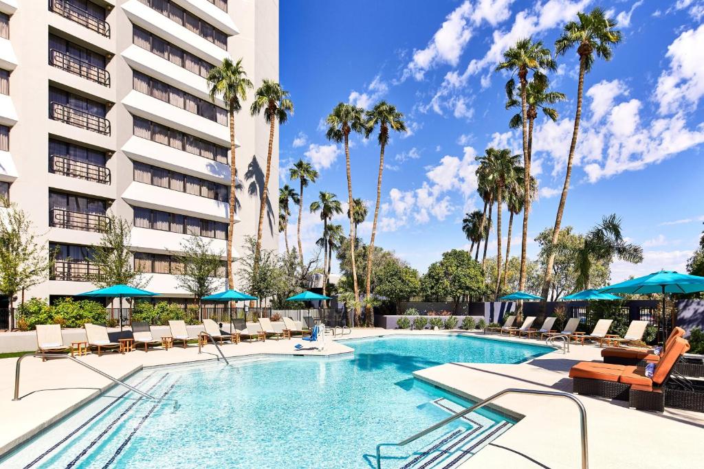 einen Pool in einem Hotel mit Stühlen und Sonnenschirmen in der Unterkunft Delta Hotels by Marriott Phoenix Mesa in Mesa