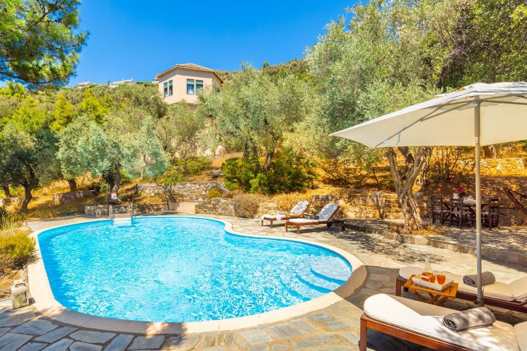 a pool with an umbrella and chairs and a house at Villa Pelago in Skopelos Town