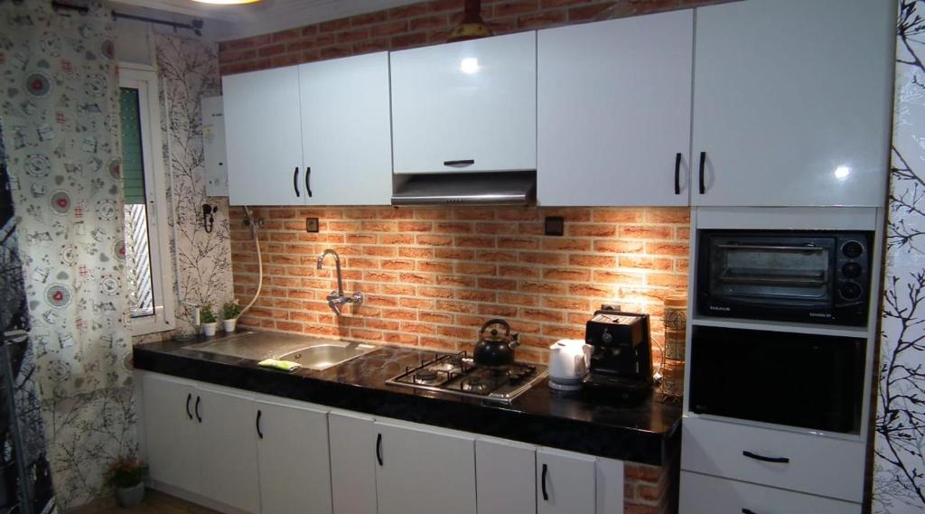 uma cozinha com armários brancos e uma parede de tijolos em StayHere, Apartment Garden View in center, Close To Beach em El Jadida