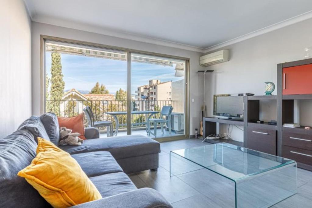 een woonkamer met een bank en een glazen tafel bij Tamanaco Beach 1BDR apartment with balcony sea view and pool in Antibes