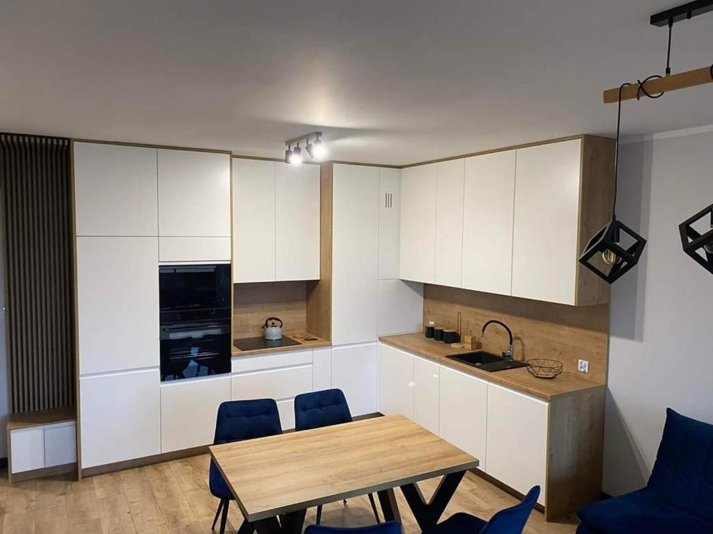 a kitchen with white cabinets and a wooden table and chairs at Nowoczesny Apartament Królowej Jadwigi in Radom