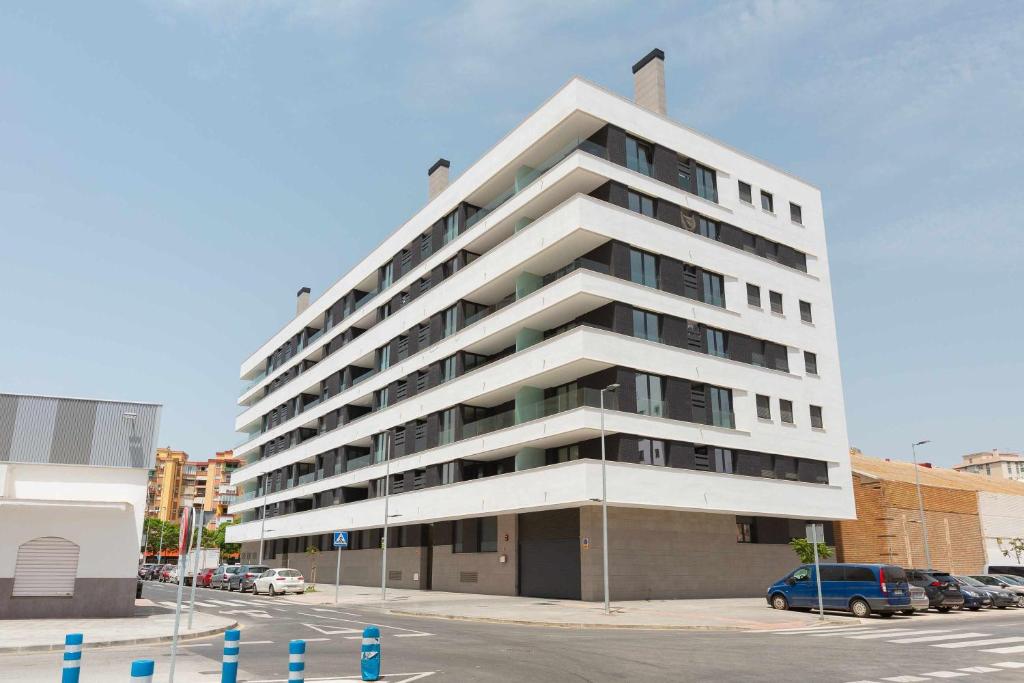 a tall white building with cars parked in a parking lot at Cosmopolitan Loft y Malaga Beach in Málaga