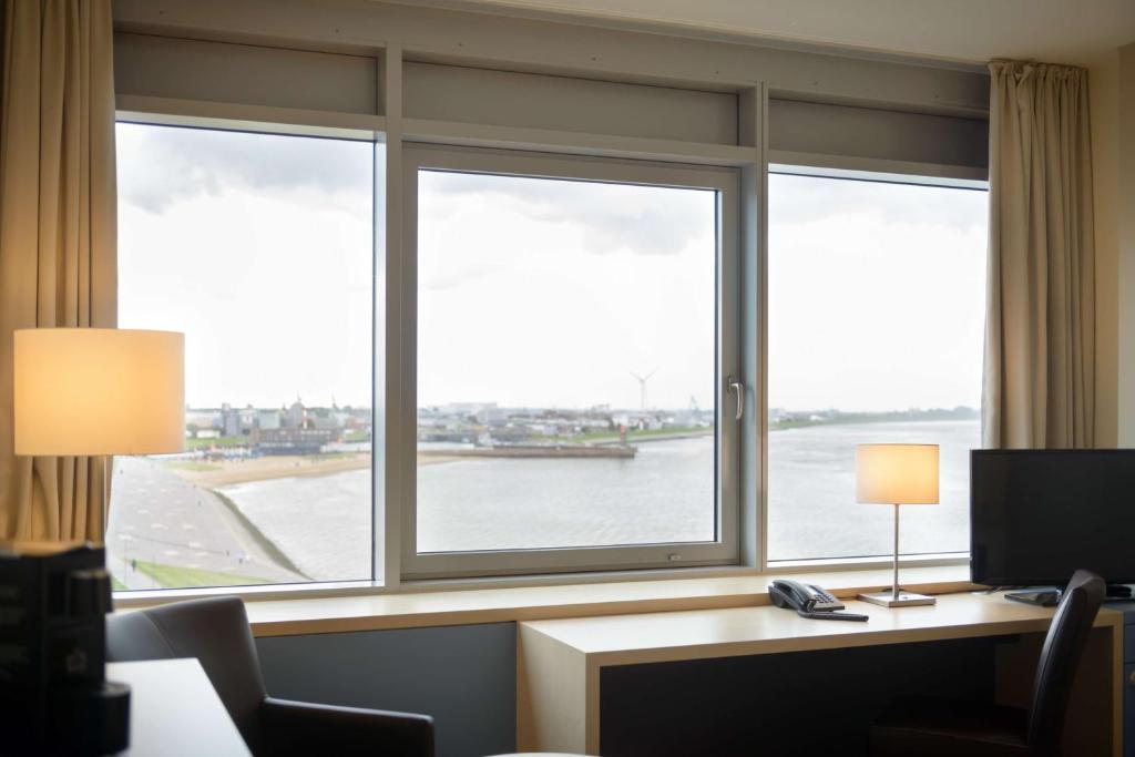 a room with three windows and a desk with a computer at Atlantic Hotel Sail City in Bremerhaven