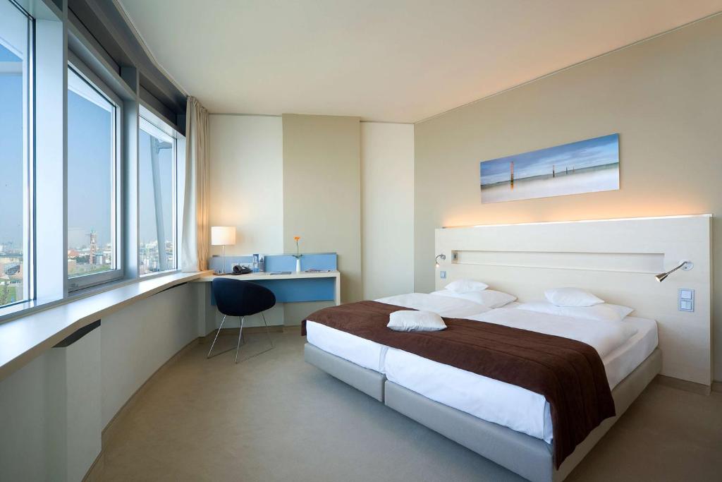 a hotel room with a bed and a desk and windows at Atlantic Hotel Sail City in Bremerhaven