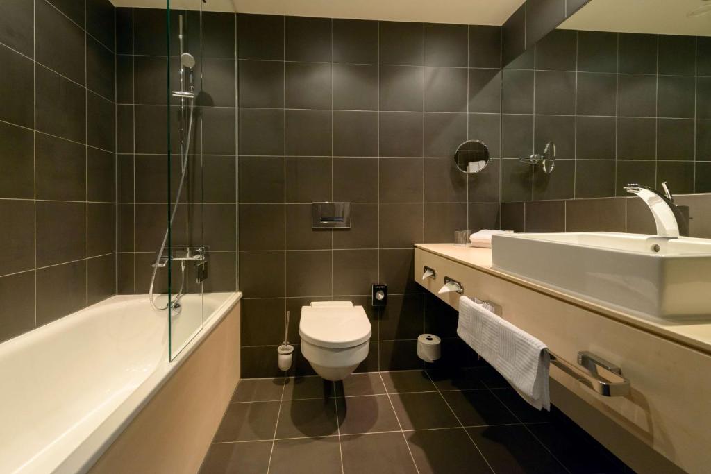 a bathroom with a sink and a toilet and a tub at Atlantic Hotel Sail City in Bremerhaven