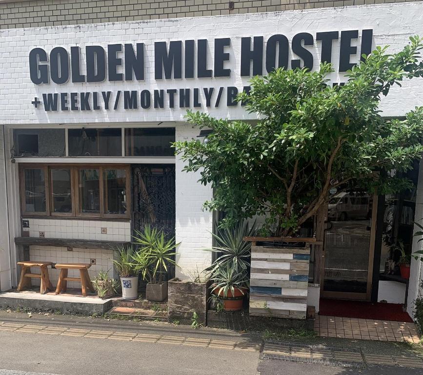 a white building with a sign for a golden mile house at Guest House Golden Mile Hostel in Amami