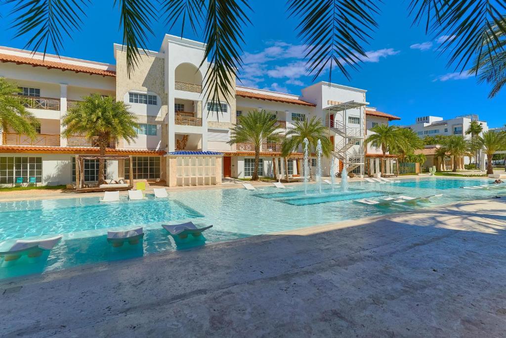a swimming pool in front of a building with palm trees at New! Lovely And Spacious Fully Equipped Condo In Cap Cana in Punta Cana