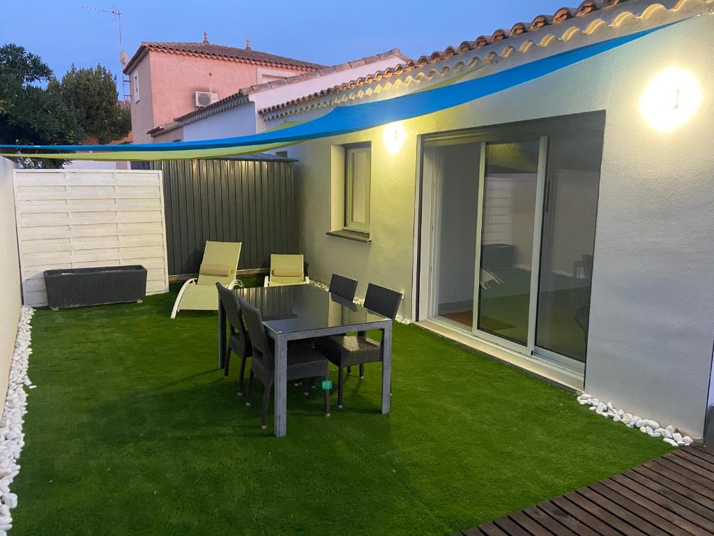 une terrasse avec une table et des chaises sur une pelouse dans l'établissement JOLIE MAISON A 700M DE LA MER, au Grau-dʼAgde