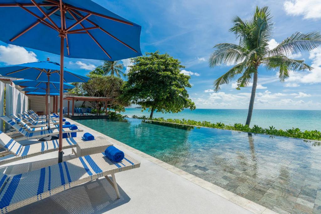 a swimming pool with chairs and umbrellas and the ocean at Synergy Samui in Chaweng