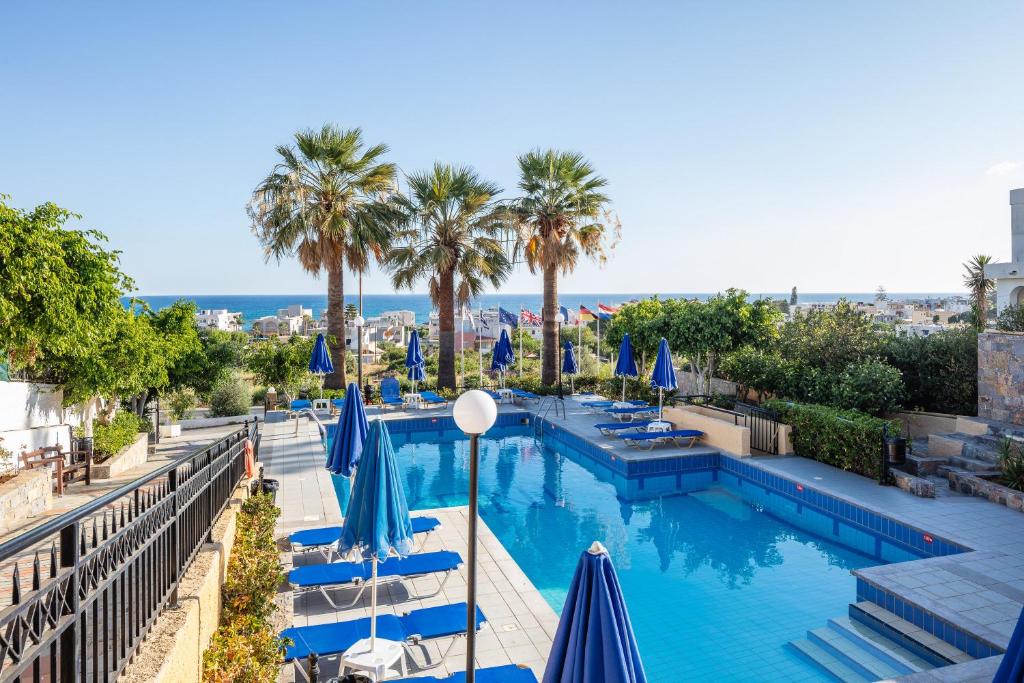 uma piscina com guarda-sóis azuis e palmeiras em Koni Village Hotel em Stalida