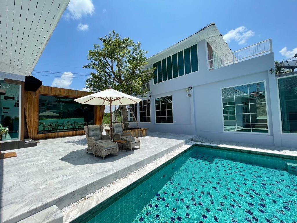 a swimming pool with two chairs and an umbrella next to a house at Skeyndor Health & Resort in Na Jomtien