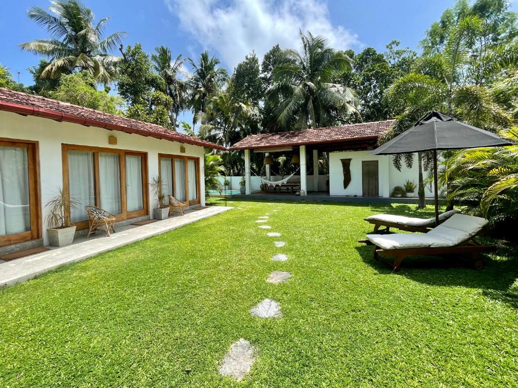 a lawn with an umbrella and a bench and a house at Kanferri Villa in Ahangama