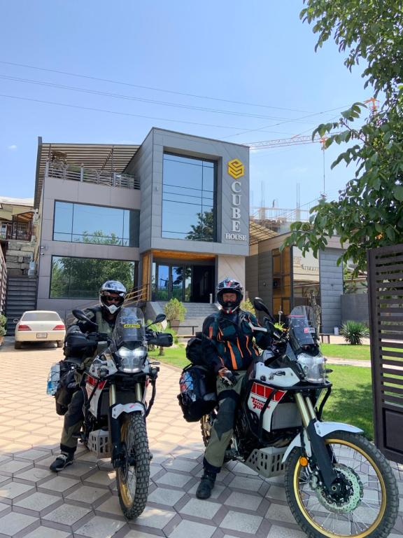 dos personas en motocicleta estacionadas frente a un edificio en Cube House Osh en Osh