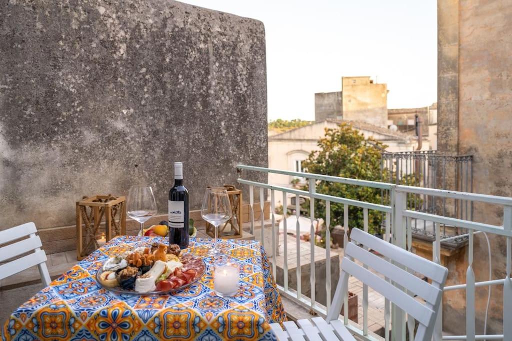 - une table avec une assiette de nourriture et de vin sur un balcon dans l'établissement Maiolica Rooms Appartamento Ragusa Ibla, à Raguse