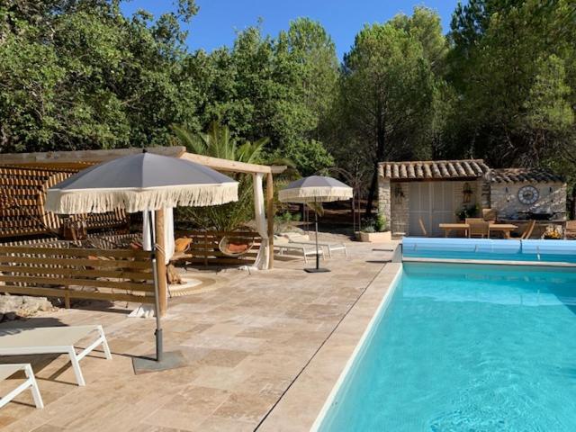 einen Pool mit Sonnenschirm, Stühlen und Tischen in der Unterkunft Le Petit Chene in Le Castellet