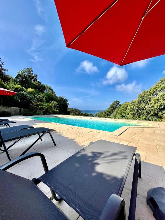 une piscine avec un parasol rouge et quelques tables et chaises dans l'établissement Domaine de Stang Bihan, à Concarneau