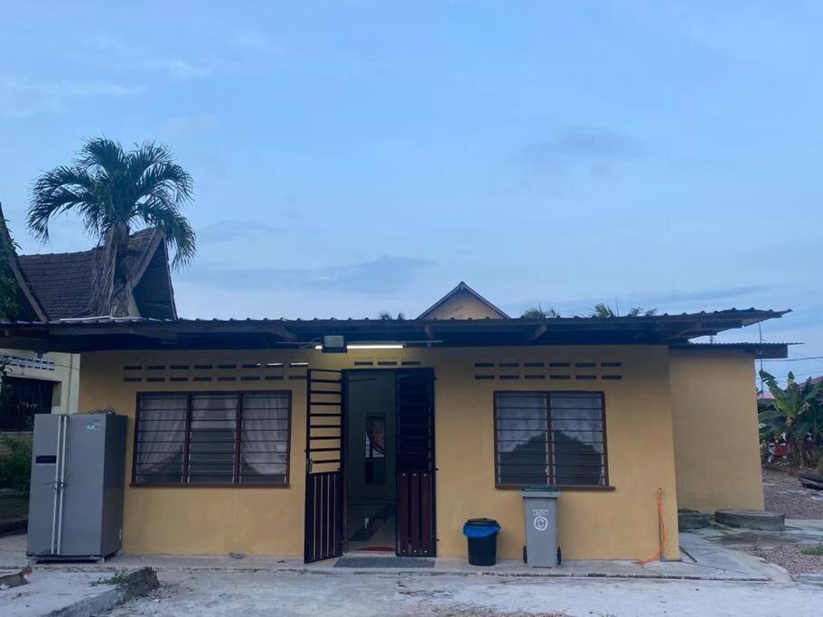 a small yellow house with a door and a palm tree at Warisan Homestay B in Mersing