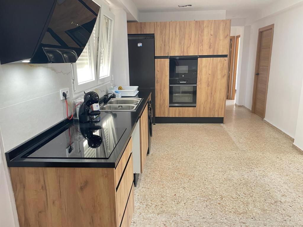 una cocina con encimera negra y armarios de madera en UIM Mediterraneo Emilio Llopis Wifi, en Sagunto