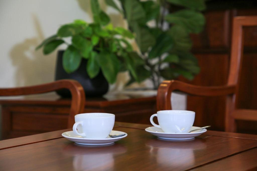 two white cups and saucers on a wooden table at Phongsavath Boutique Hotel in Vientiane