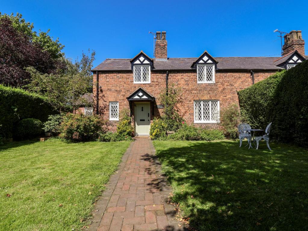 ein Backsteinhaus mit einer weißen Tür und einem Rasenplatz in der Unterkunft Jasmine Cottage in Chester