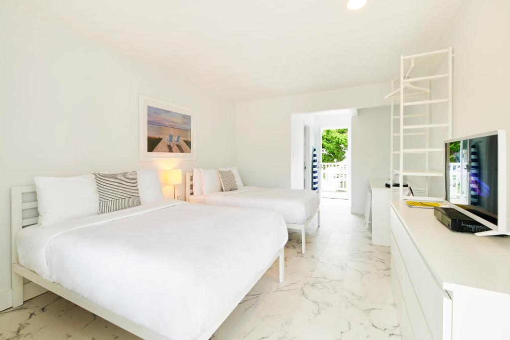 a white bedroom with two beds and a tv at The Sunset Montauk in Montauk