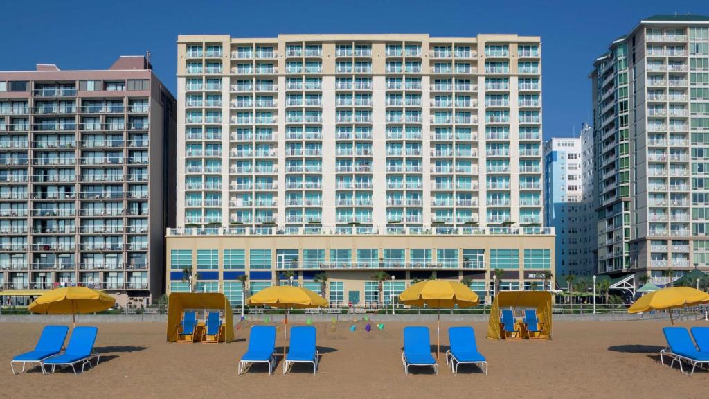 a beach with chairs and umbrellas in front of a building at Hilton Garden Inn Virginia Beach Oceanfront in Virginia Beach