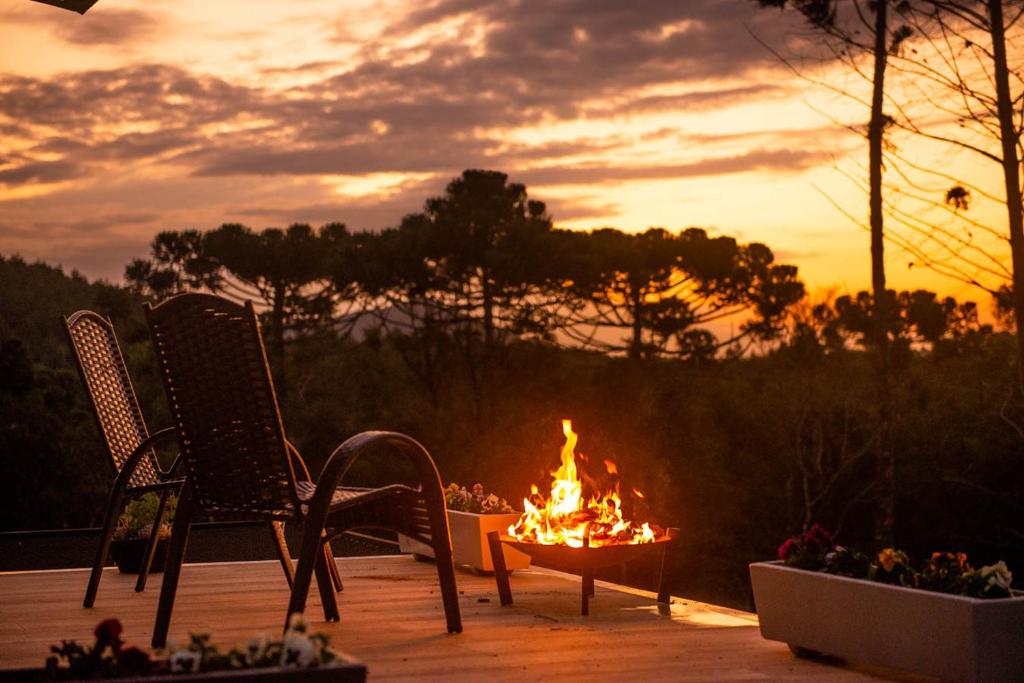 a fire pit with two chairs and a table with a fire burns at Timber Lodge Camanducaia in Monte Verde
