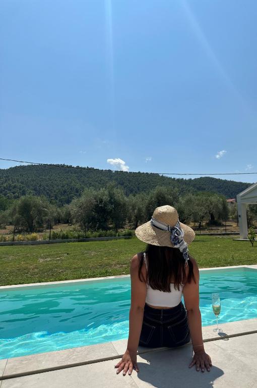 a woman in a hat sitting next to a swimming pool at Astrum Luxury Suites in Vourvourou