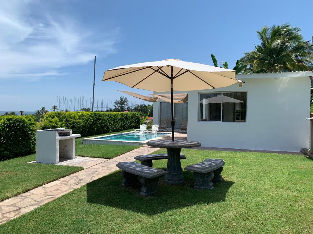 uma mesa e bancos com um guarda-sol ao lado de uma piscina em Tropical Vibes Beach House em San Rafael