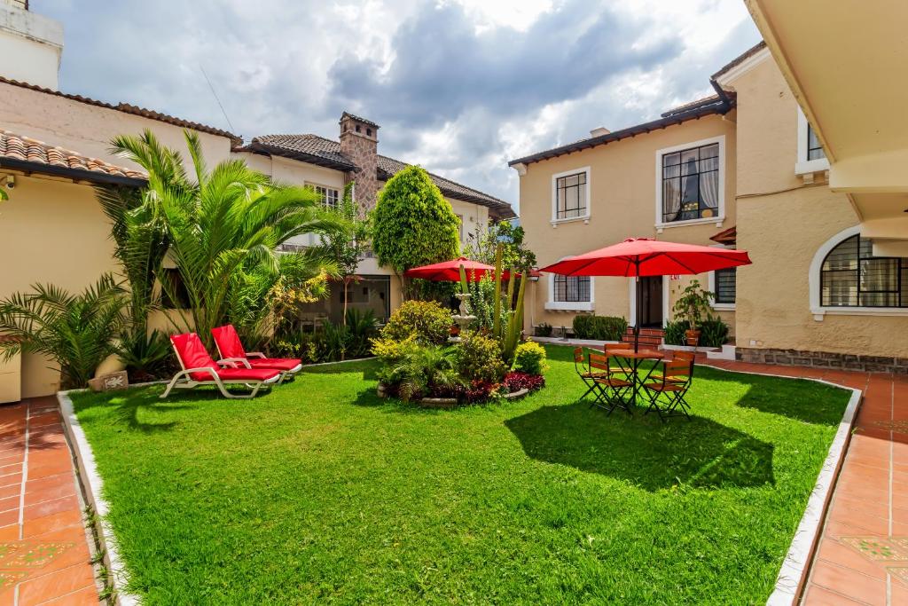 un patio con sillas rojas y sombrilla en Hotel La Cartuja, en Quito