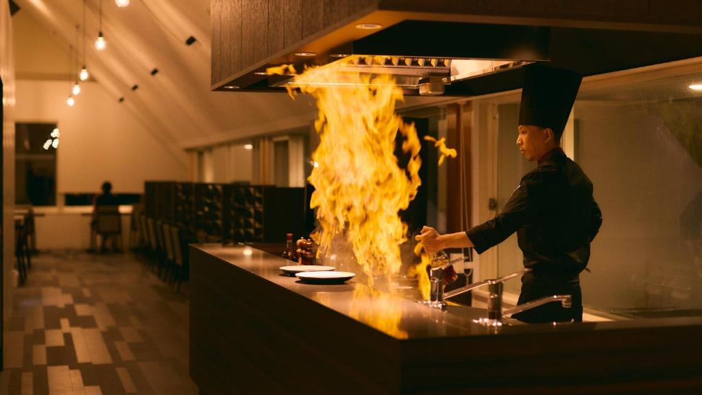 a chef cooking in a kitchen with fire on the counter at Fourtreat Kusatsu in Kusatsu
