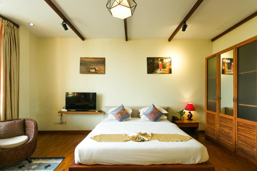 ein Schlafzimmer mit einem Bett, einem Stuhl und einem TV in der Unterkunft Ambassador Hill in Yangon