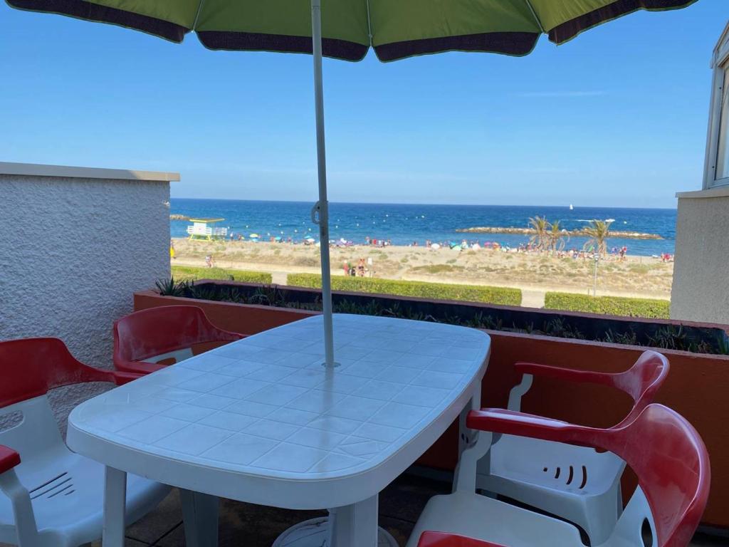 - une table et des chaises avec un parasol et la plage dans l'établissement Appart cosy 4 pers, 1 ch, plage, parking privé - FR-1-81-526, au Barcarès