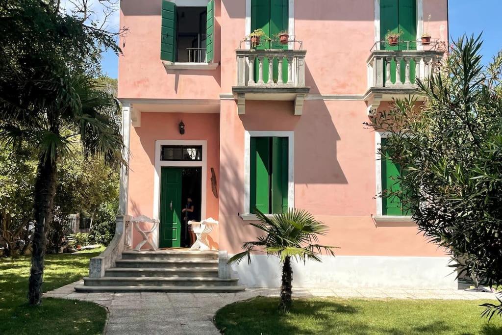 um edifício cor-de-rosa com janelas verdes e uma porta em Venezia Lido Villa Delle Palme em Lido di Venezia
