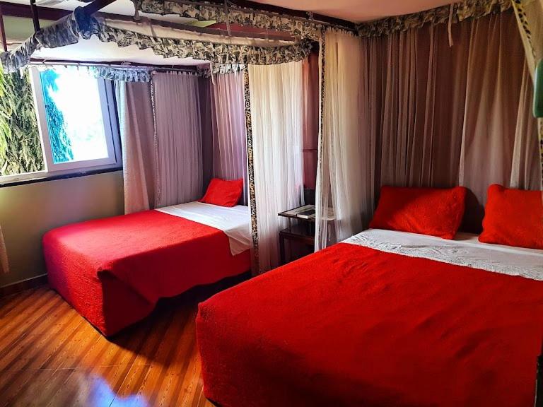 1 dormitorio con 2 camas con sábanas rojas y ventana en Hotel Basilea Mtwapa, en Mtwapa