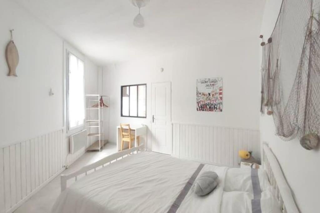 a white bedroom with a bed and a window at La Coquille in Sète