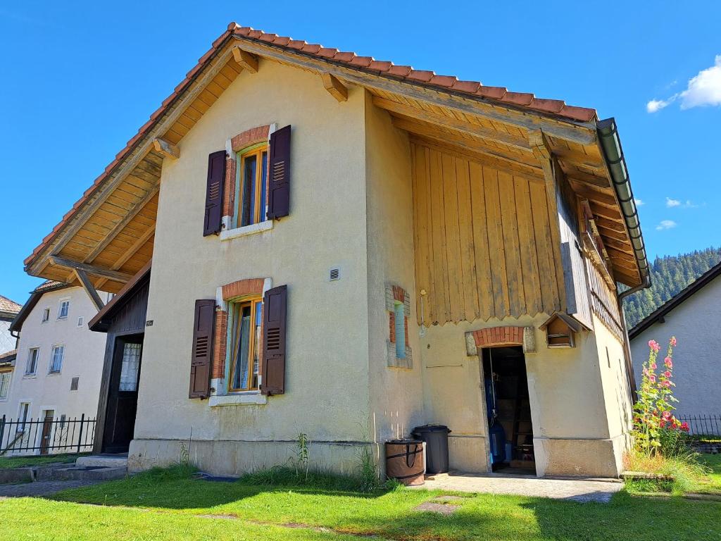 uma pequena casa branca com janelas castanhas com persianas em Charmante maison individuelle em Les Verrières