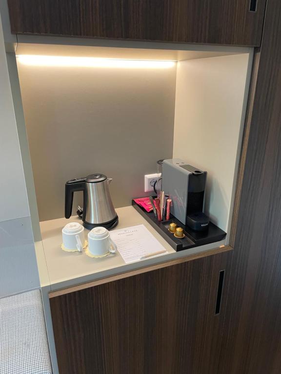 a room with a coffee maker and two cups on a shelf at Hotel Monvillage in Mondercange