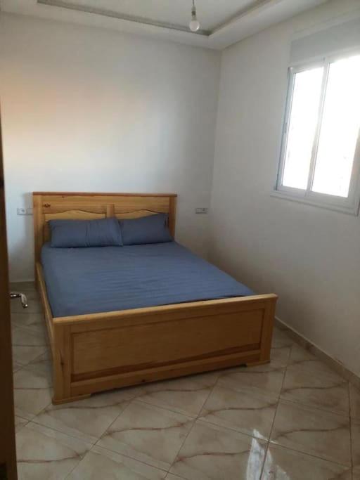 um quarto com uma cama com lençóis azuis e uma janela em Asonfo em Aourir