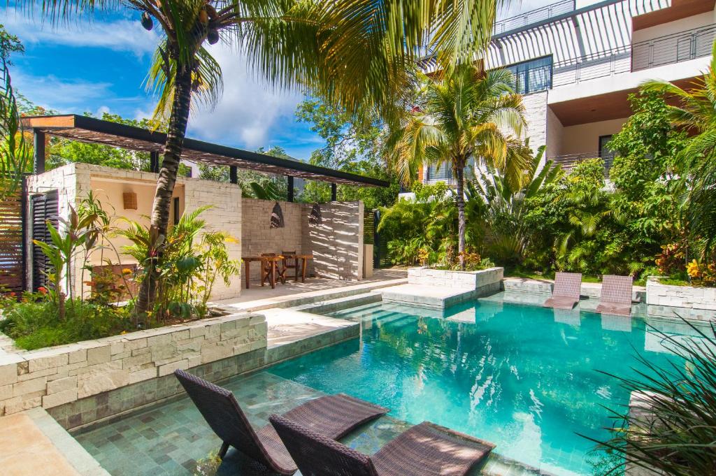 an outdoor swimming pool with chairs and a house at Naj Kiin- Aldea Zama Tulum by Casago in Tulum