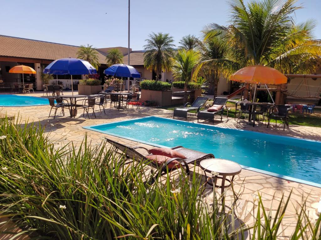 una piscina con mesas, sillas y sombrillas en Hotel Pousada Parque das Águas en Olímpia