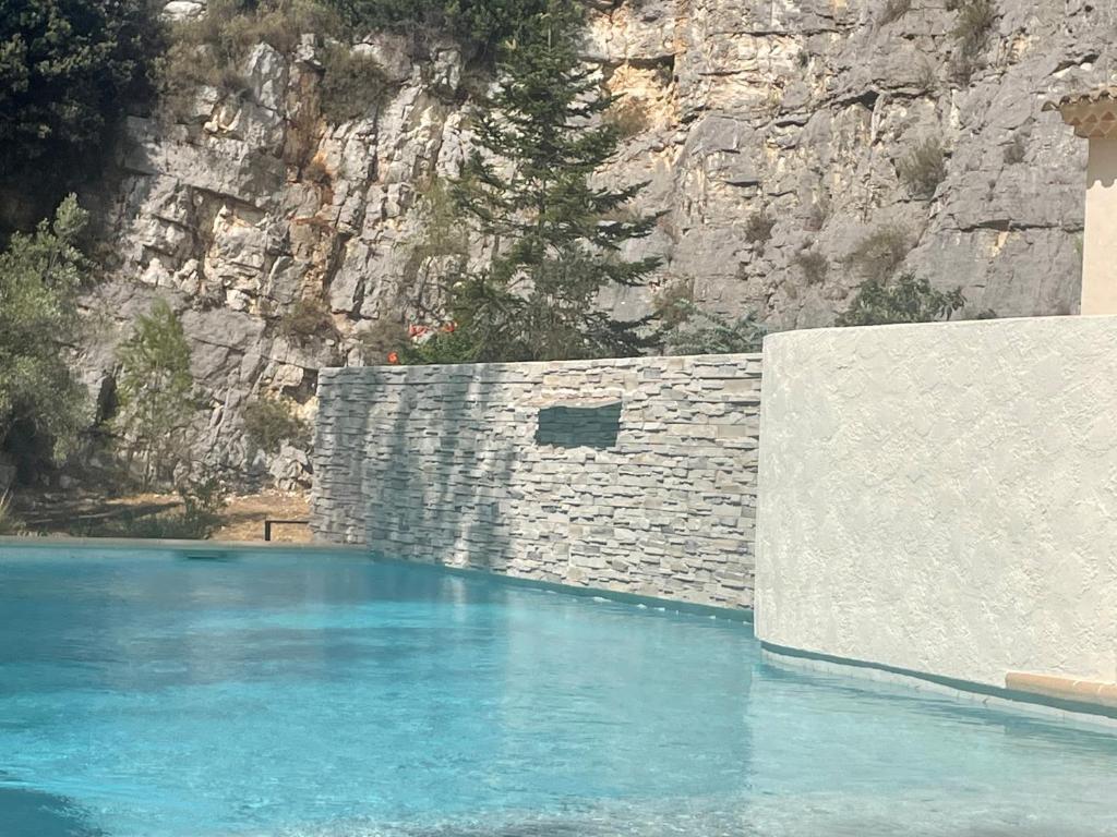 een zwembad met een stenen muur en blauw water bij La villa des Carriers- maison avec piscine proche mer in Roquefort-les-Pins