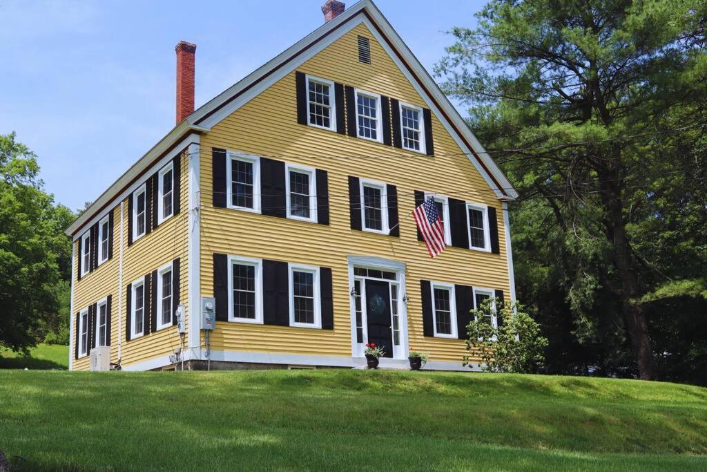 a large yellow house with an american flag on it at Hillside Haven: Luxe Farm Escape - 5BR-2 King Beds in Swanzey