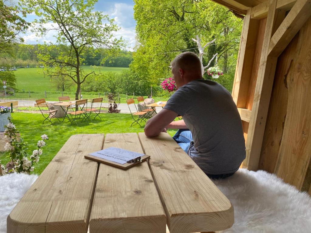 a man sitting at a wooden table with a book at Bauerngarten in Hofgeismar