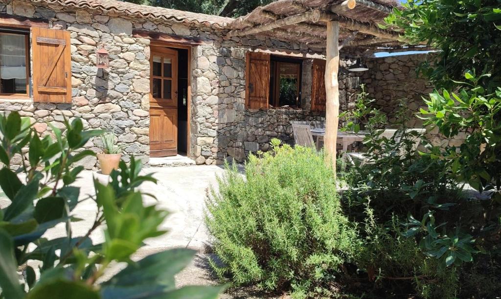 une maison en pierre avec une porte en bois dans un jardin dans l'établissement Les Bergeries de Piazzagina, à Piediquarcio