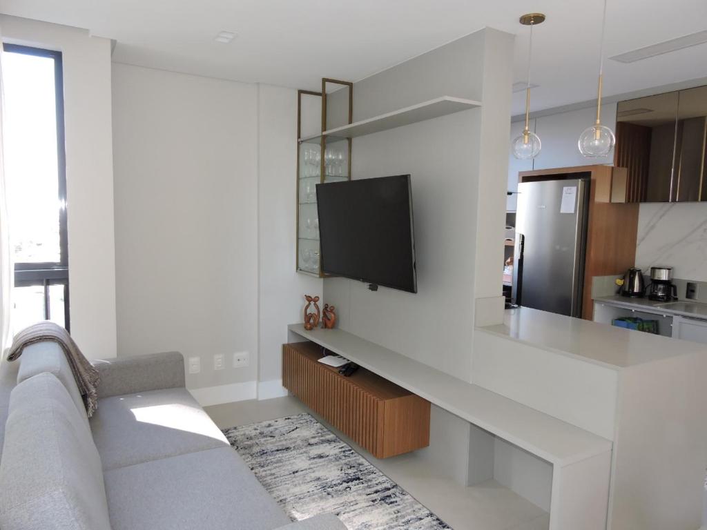 a white living room with a couch and a tv at Apart moderno 3 suites 2 vagas de garagem e quadra do mar in Itapema