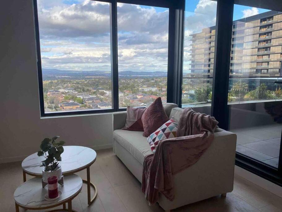 a living room with a couch and large windows at Top Floor Mountain View Luxury Rental Unit in SkyGarden Glen in Glen Waverley