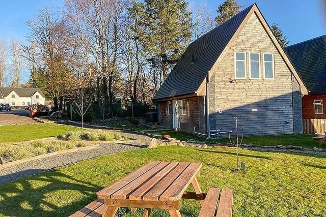 un banco de madera sentado en el césped frente a una casa en Pheasant lodge - Balmaha 3 bed en Glasgow