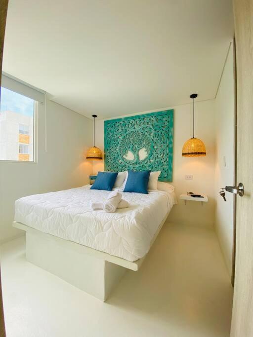 a white bedroom with a large bed with blue pillows at Espectacular Apartamento Jerusalema Villeta in Villeta
